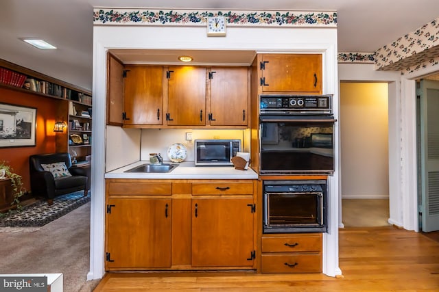 kitchen with light countertops, stainless steel microwave, brown cabinetry, light wood-style floors, and a sink