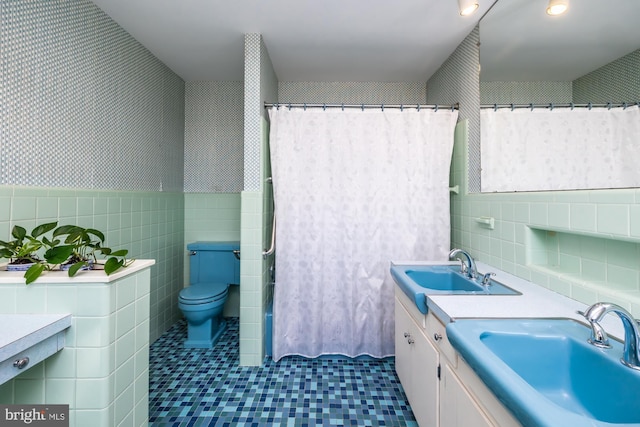 full bathroom featuring a sink, tile walls, toilet, and double vanity