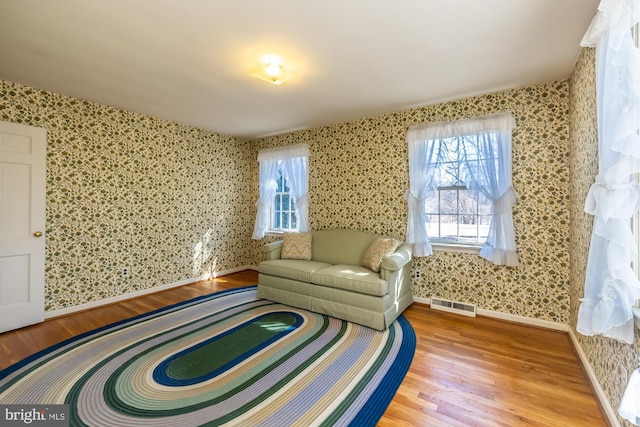 sitting room featuring wallpapered walls, baseboards, visible vents, and wood finished floors