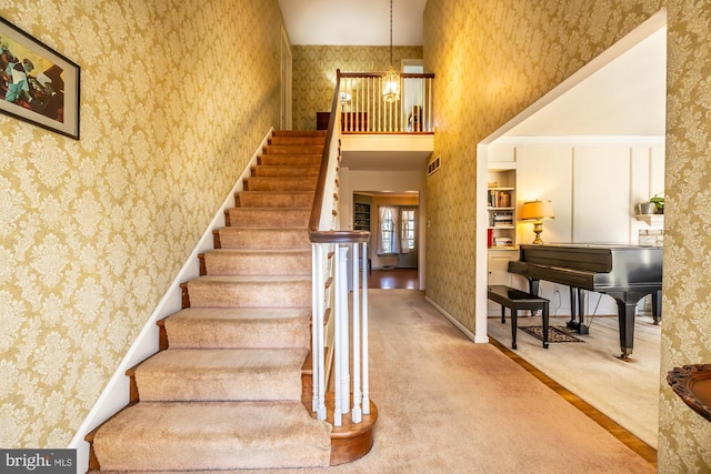 stairs with a high ceiling, carpet, and wallpapered walls