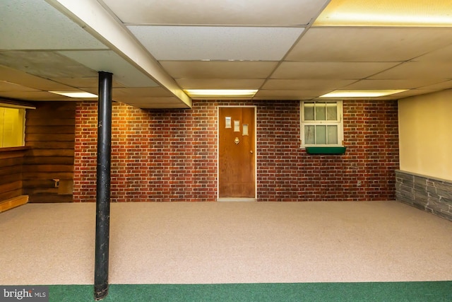 finished below grade area featuring carpet, a drop ceiling, and brick wall