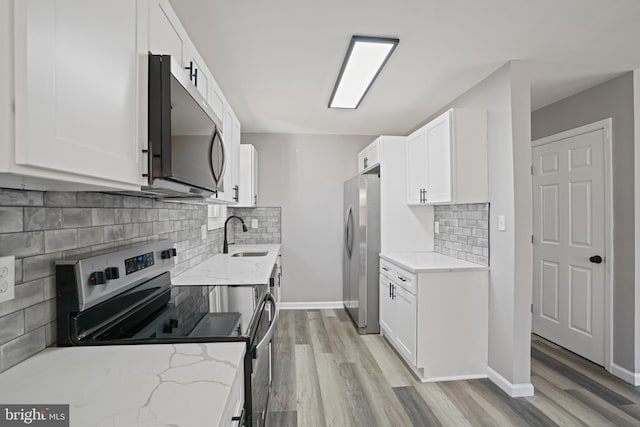 kitchen with appliances with stainless steel finishes, white cabinets, a sink, and light stone countertops