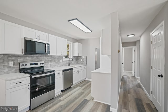 kitchen featuring stainless steel appliances, white cabinetry, light wood-style floors, backsplash, and light stone countertops