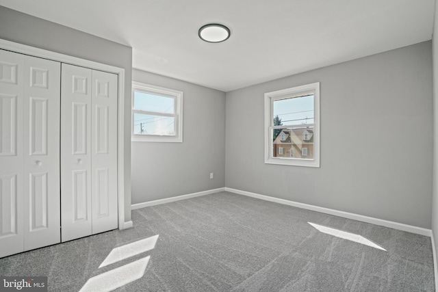 unfurnished bedroom with multiple windows, baseboards, a closet, and carpet flooring