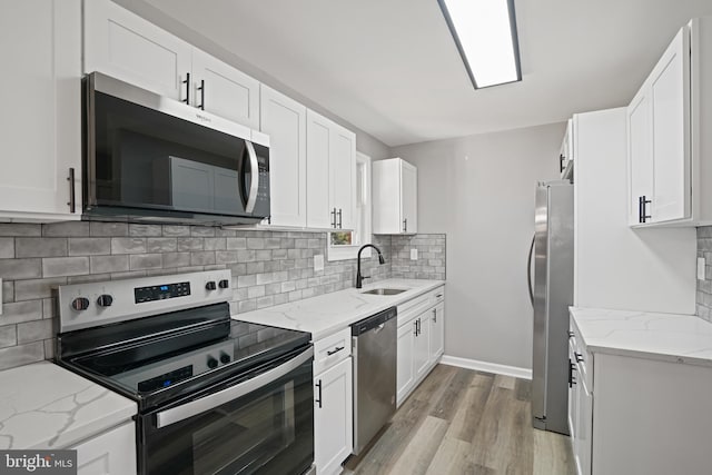 kitchen featuring stainless steel appliances, white cabinets, a sink, and light stone countertops