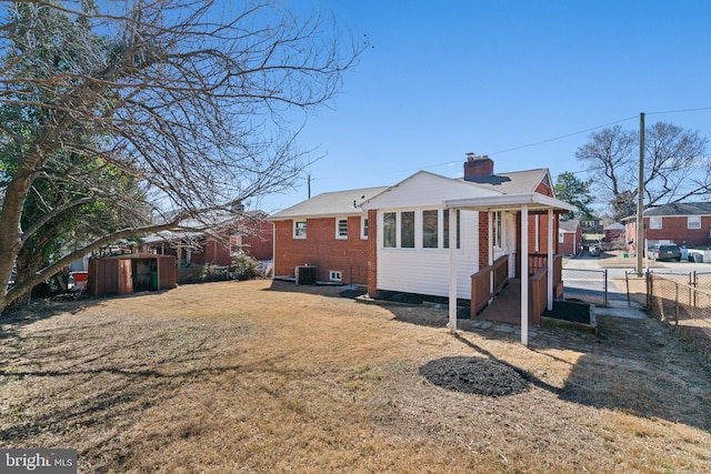 back of house with a lawn, a chimney, fence, central air condition unit, and brick siding