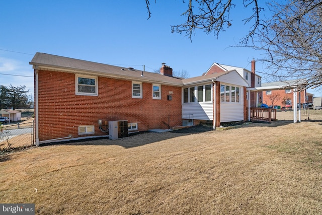 rear view of property with cooling unit, brick siding, fence, and a lawn