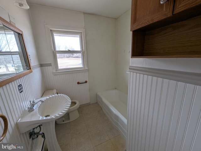 full bath with toilet, tile patterned floors, a washtub, and wainscoting