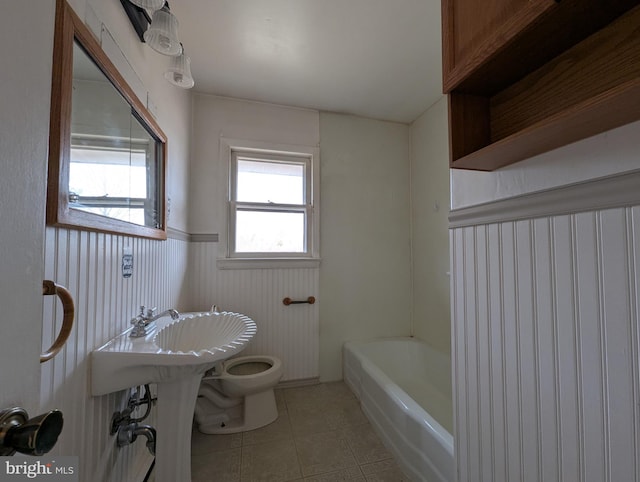 full bathroom featuring a washtub, tile patterned flooring, wainscoting, and toilet