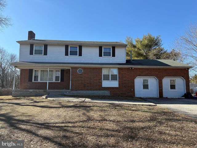 traditional-style home with driveway, brick siding, a chimney, and a front lawn