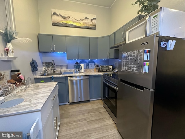 kitchen featuring light wood finished floors, light countertops, appliances with stainless steel finishes, and a sink