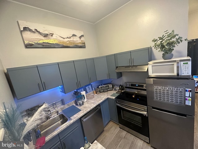 kitchen featuring a toaster, light countertops, appliances with stainless steel finishes, light wood-style floors, and under cabinet range hood