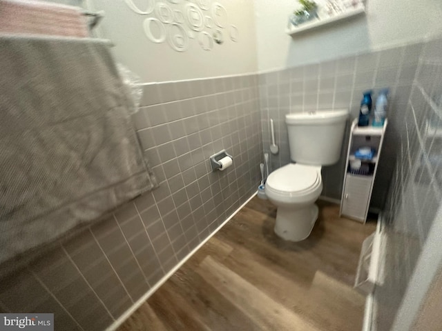 bathroom featuring toilet, a wainscoted wall, tile walls, and wood finished floors