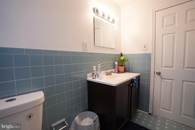 bathroom with toilet, wainscoting, tile walls, and vanity