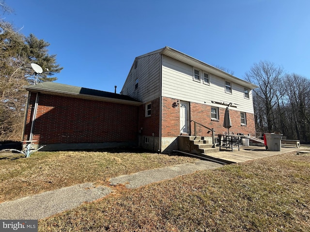 back of house featuring entry steps, a patio area, brick siding, and a lawn