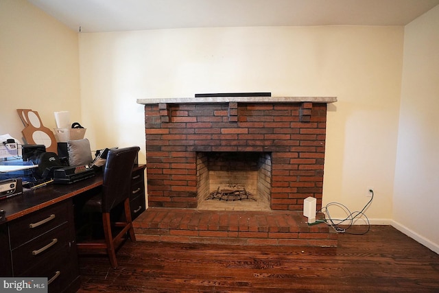 office area featuring dark wood-style floors, a brick fireplace, and baseboards