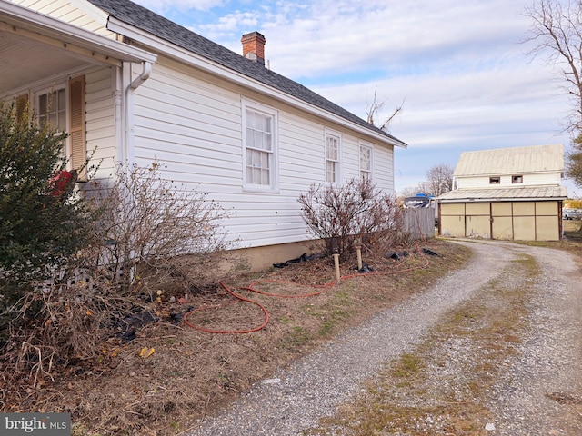 view of property exterior with roof with shingles, dirt driveway, and a chimney