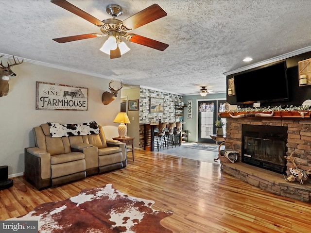 living room with a textured ceiling, wood finished floors, crown molding, and a stone fireplace