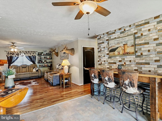 living room featuring ornamental molding, ceiling fan, a textured ceiling, wood finished floors, and baseboards