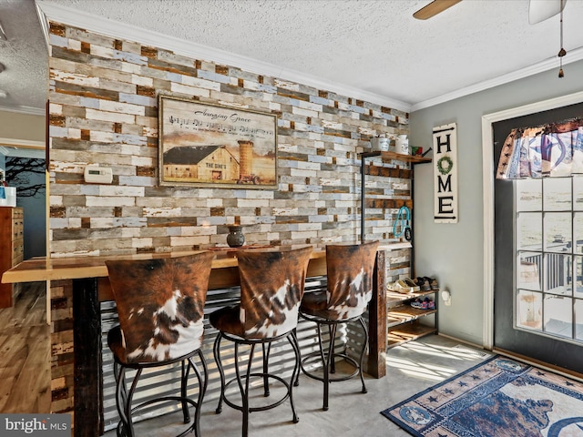 bar with a ceiling fan, concrete floors, ornamental molding, and a textured ceiling