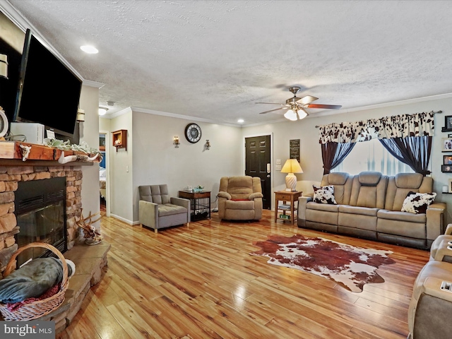 living room featuring hardwood / wood-style flooring, ceiling fan, a stone fireplace, crown molding, and a textured ceiling