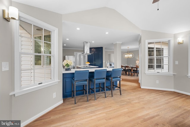 kitchen with blue cabinets, a kitchen breakfast bar, vaulted ceiling, baseboards, and light wood-type flooring