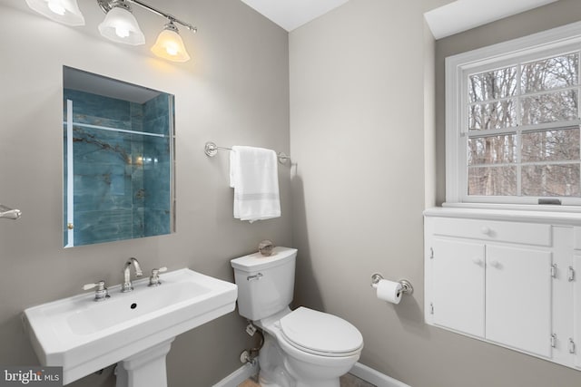 bathroom with baseboards, a healthy amount of sunlight, a sink, and toilet