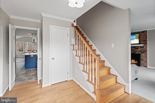 stairs with a brick fireplace, crown molding, baseboards, and wood finished floors