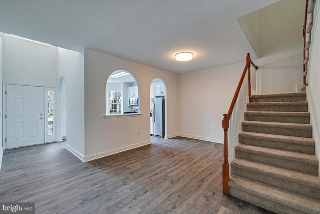 entryway featuring stairs, baseboards, arched walkways, and dark wood-style flooring