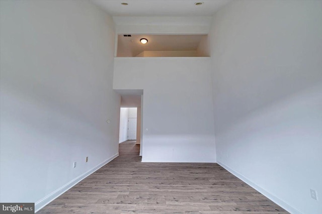 interior space with light wood-type flooring, a towering ceiling, and baseboards