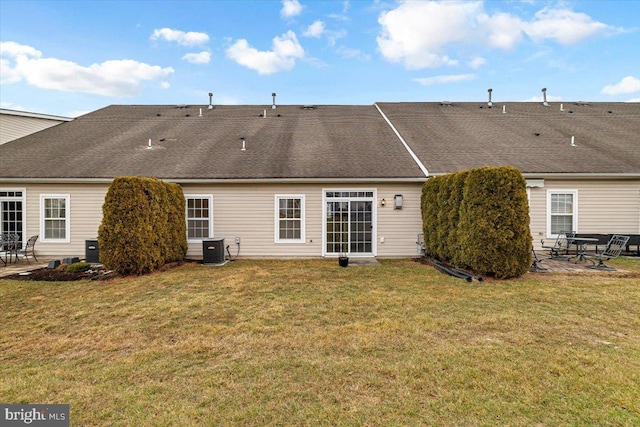 rear view of house with central AC, a shingled roof, a lawn, and a patio