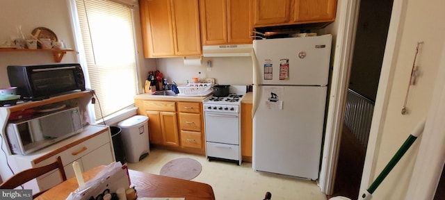 kitchen with brown cabinets, light floors, light countertops, white appliances, and under cabinet range hood