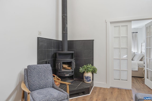 sitting room with wood finished floors, a wood stove, and french doors