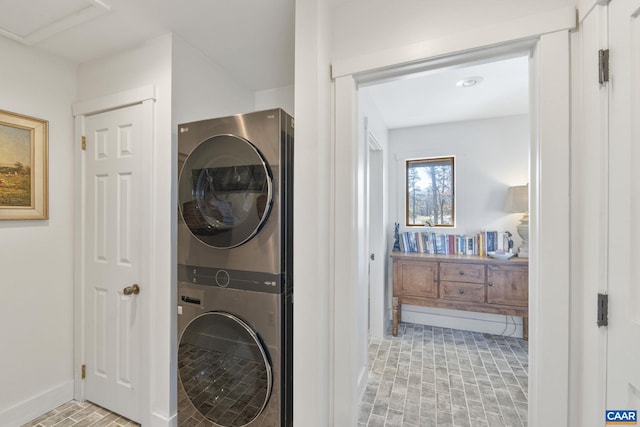 laundry room featuring stacked washer / drying machine, brick floor, laundry area, and baseboards