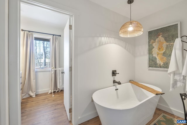 bathroom featuring wood finished floors, baseboards, and a freestanding bath