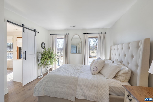 bedroom featuring light wood-style flooring, visible vents, and a barn door