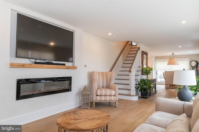 living room with light wood-style flooring, recessed lighting, stairway, and a glass covered fireplace