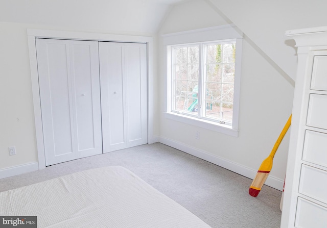 unfurnished bedroom featuring lofted ceiling, a closet, light carpet, and baseboards