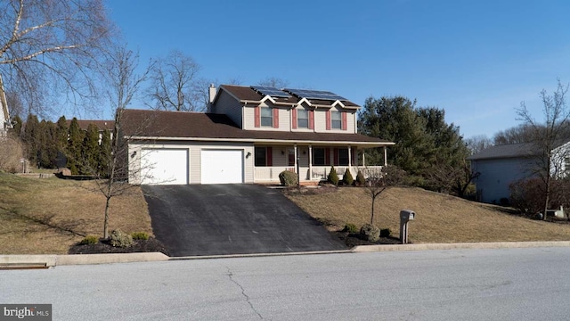 traditional-style house featuring aphalt driveway, solar panels, an attached garage, and covered porch