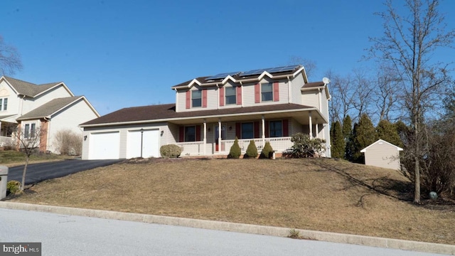 traditional-style house featuring roof mounted solar panels, covered porch, an attached garage, a front yard, and driveway