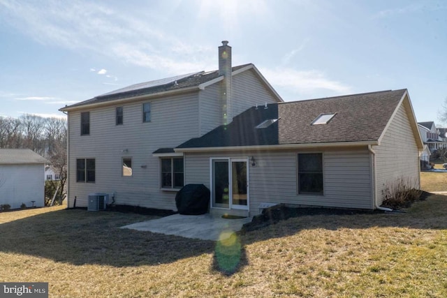 rear view of house featuring central AC, a chimney, a patio area, a yard, and a shingled roof