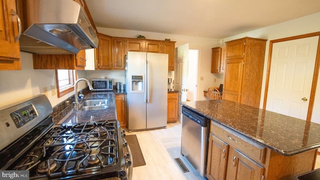 kitchen with a center island, brown cabinets, appliances with stainless steel finishes, range hood, and a sink