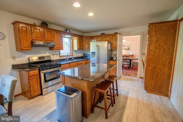 kitchen featuring a center island, appliances with stainless steel finishes, under cabinet range hood, and brown cabinetry