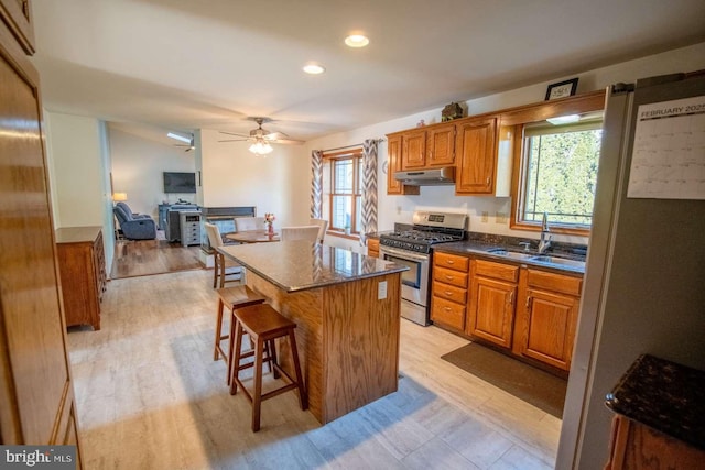 kitchen featuring a kitchen island, stainless steel range with gas stovetop, under cabinet range hood, brown cabinets, and a sink