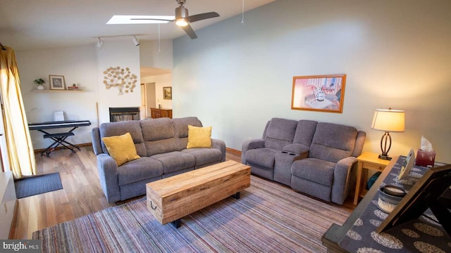 living room featuring wood finished floors, high vaulted ceiling, a glass covered fireplace, baseboards, and a ceiling fan