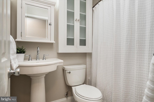 bathroom featuring toilet, a shower with curtain, and baseboards