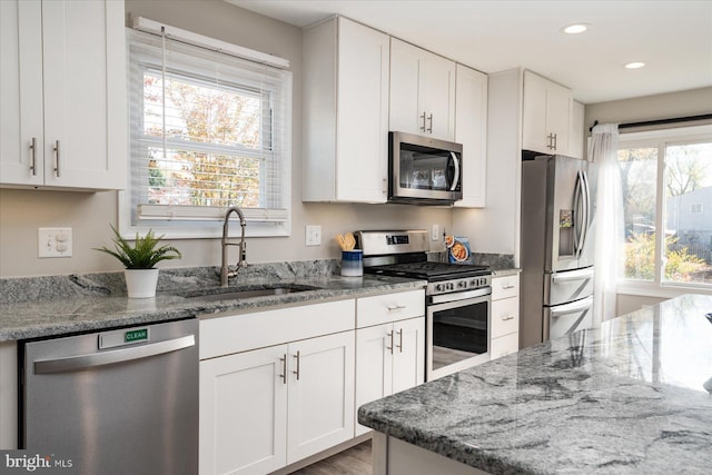 kitchen with appliances with stainless steel finishes, white cabinets, a sink, and light stone counters