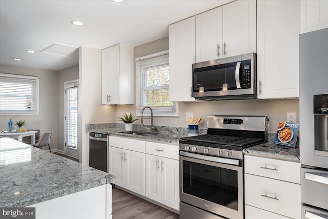 kitchen featuring light stone countertops, light wood-style flooring, stainless steel appliances, white cabinetry, and a sink