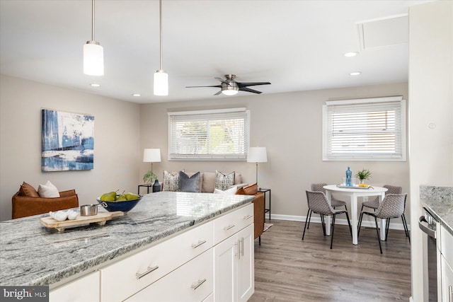 kitchen with light wood-style flooring, white cabinets, hanging light fixtures, and light stone counters