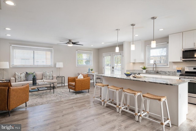 kitchen with appliances with stainless steel finishes, pendant lighting, light stone counters, white cabinetry, and a kitchen island